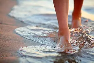 Nahaufnahme von Füßen, die am Strand durch Wasser laufen